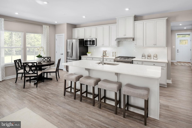 kitchen featuring stainless steel appliances, sink, a center island with sink, light hardwood / wood-style flooring, and white cabinetry