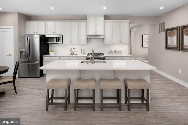 kitchen with white cabinets, stainless steel appliances, a kitchen island with sink, and sink