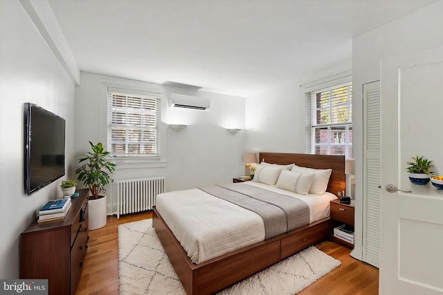 bedroom with a wall unit AC, light wood-type flooring, and radiator