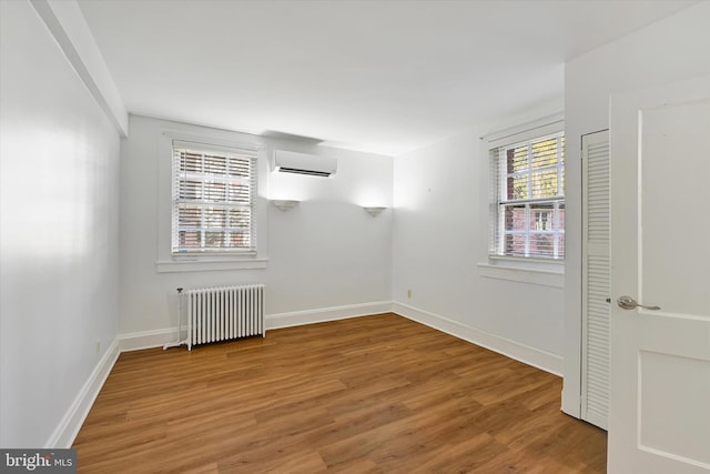 empty room featuring a wall unit AC, radiator, and hardwood / wood-style floors