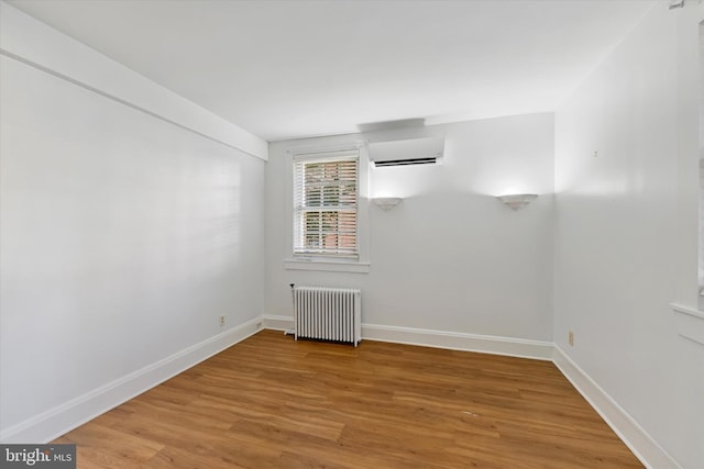 spare room featuring wood-type flooring, radiator, and a wall mounted AC