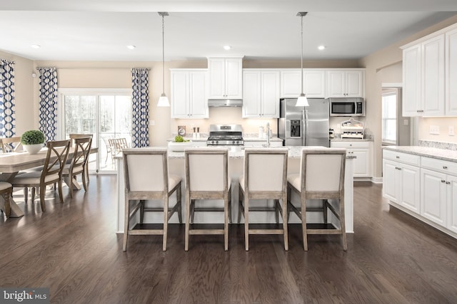 kitchen featuring white cabinetry, hanging light fixtures, dark hardwood / wood-style floors, a center island with sink, and appliances with stainless steel finishes