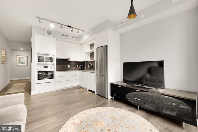 kitchen featuring white cabinetry, sink, light hardwood / wood-style flooring, decorative light fixtures, and appliances with stainless steel finishes