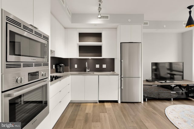 kitchen with white cabinets, sink, light wood-type flooring, appliances with stainless steel finishes, and tasteful backsplash