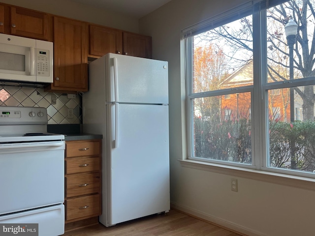 kitchen with backsplash, a wealth of natural light, light hardwood / wood-style flooring, and white appliances