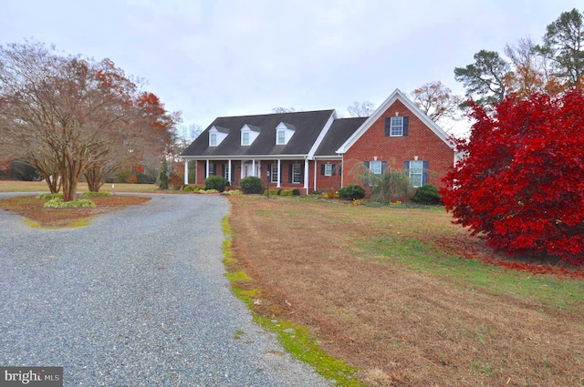 new england style home featuring covered porch and a front lawn