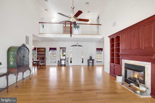 living room featuring ceiling fan, light hardwood / wood-style floors, a premium fireplace, and a high ceiling