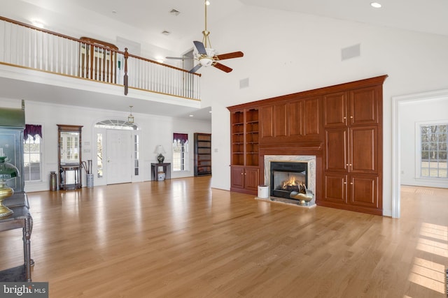 unfurnished living room with a high end fireplace, ceiling fan, high vaulted ceiling, and light hardwood / wood-style flooring