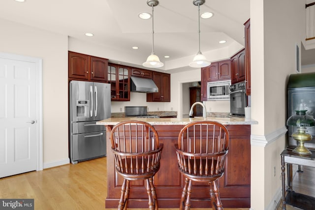 kitchen featuring black appliances, a kitchen breakfast bar, light hardwood / wood-style flooring, light stone counters, and kitchen peninsula