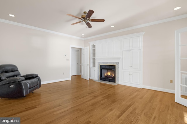 unfurnished living room with a high end fireplace, crown molding, ceiling fan, and light wood-type flooring