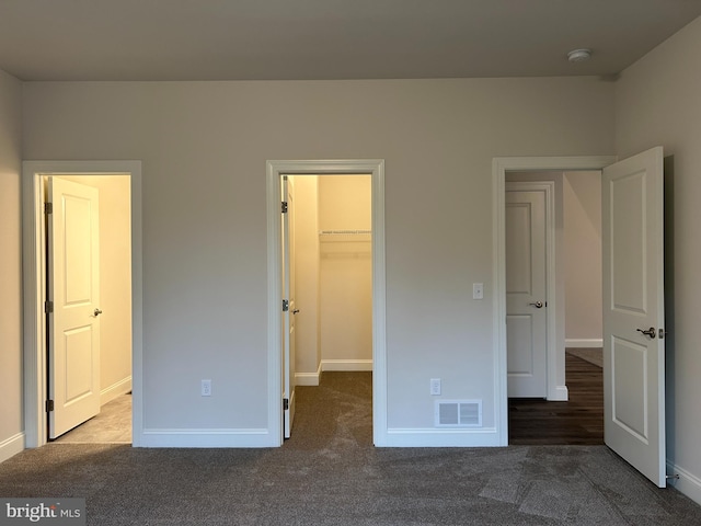 unfurnished bedroom featuring a walk in closet, dark carpet, and a closet