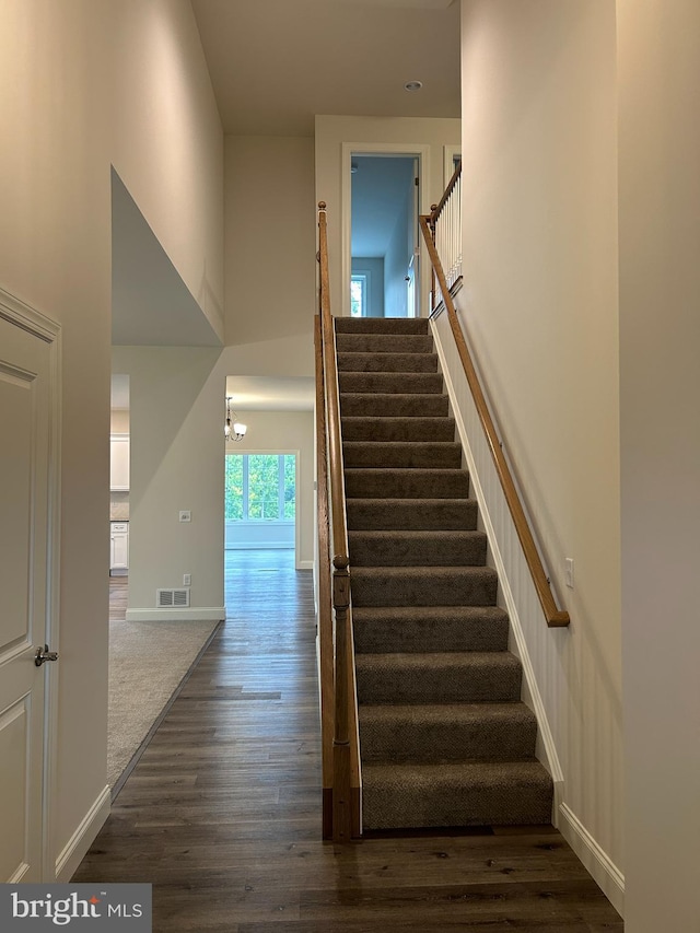 stairs featuring wood-type flooring, a notable chandelier, and a high ceiling