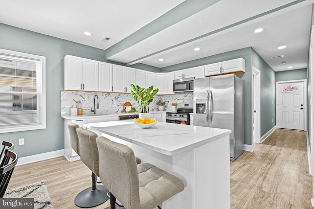 kitchen with backsplash, white cabinets, stainless steel appliances, and light hardwood / wood-style floors