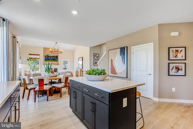 kitchen with a center island, hanging light fixtures, a kitchen breakfast bar, a notable chandelier, and light wood-type flooring