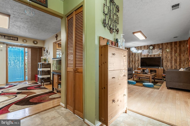 hallway featuring a textured ceiling, light hardwood / wood-style floors, and wooden walls