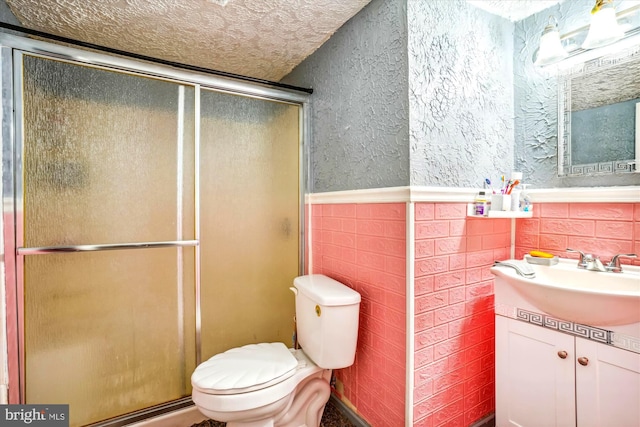 bathroom with vanity, a shower with door, toilet, a textured ceiling, and tile walls