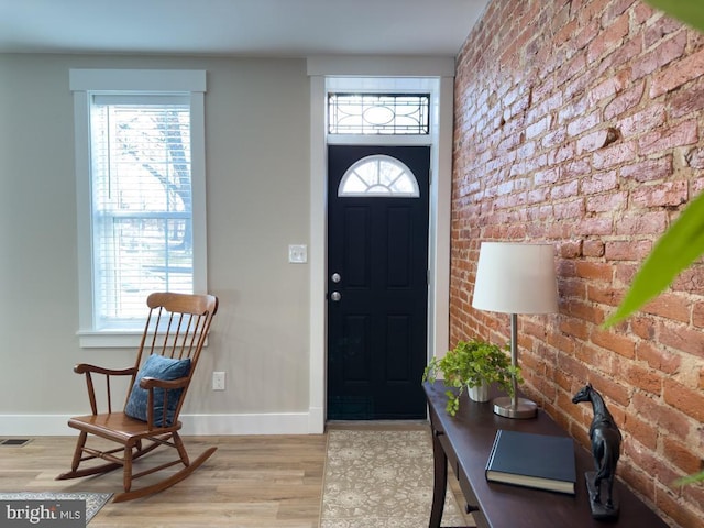 foyer entrance with light hardwood / wood-style floors, plenty of natural light, and brick wall