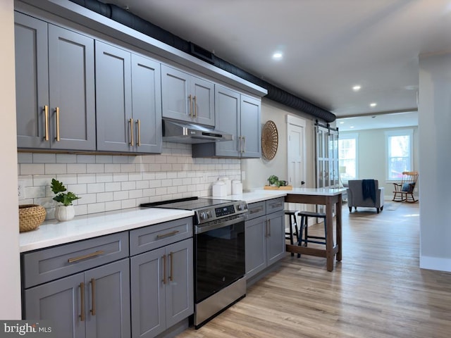 kitchen with backsplash, gray cabinets, stainless steel stove, and light wood-type flooring