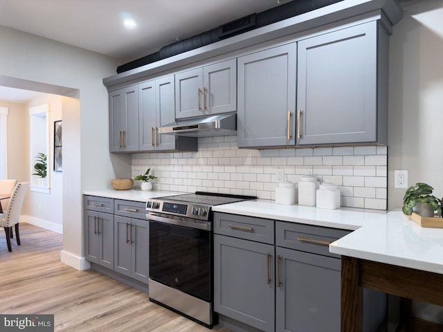 kitchen with gray cabinets, stainless steel range oven, light wood-type flooring, and backsplash