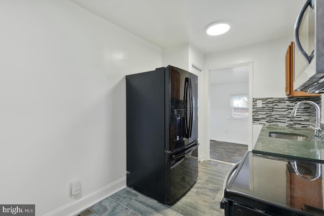 kitchen featuring backsplash, black refrigerator with ice dispenser, sink, and stove