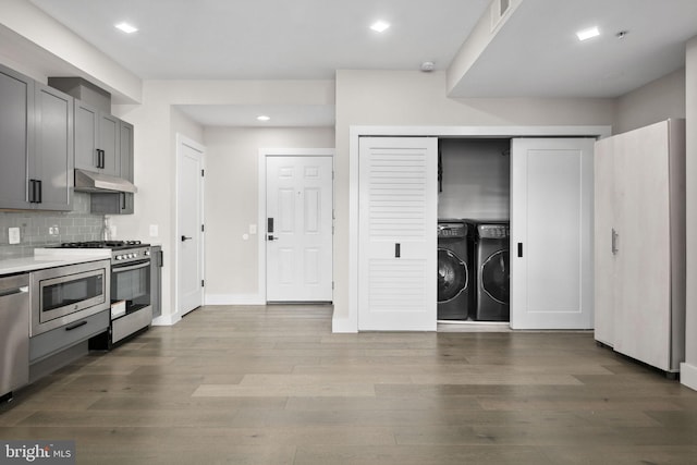 1028 Bladensburg Rd NE Unit 38, Washington, DC 20002 - kitchen with washing machine and clothes dryer, stainless steel appliances, under cabinet range hood, tasteful backsplash, and wood finished floors