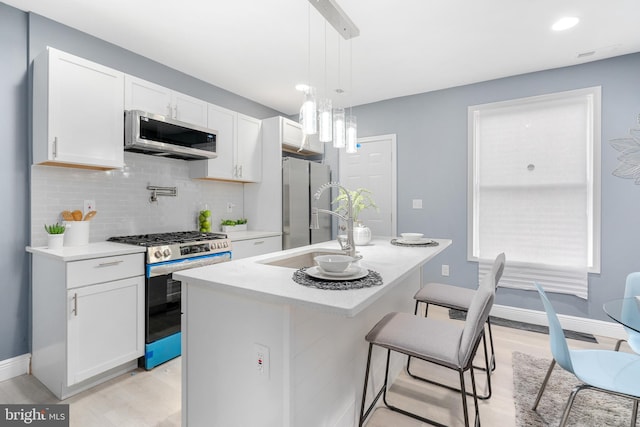 kitchen featuring white cabinets, appliances with stainless steel finishes, decorative light fixtures, and a kitchen island with sink