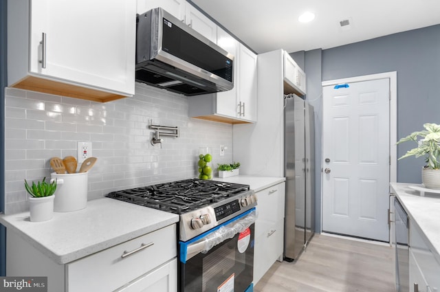 kitchen featuring decorative backsplash, white cabinetry, light wood-type flooring, and appliances with stainless steel finishes