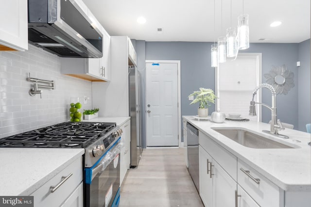 kitchen with appliances with stainless steel finishes, sink, white cabinets, light hardwood / wood-style floors, and hanging light fixtures