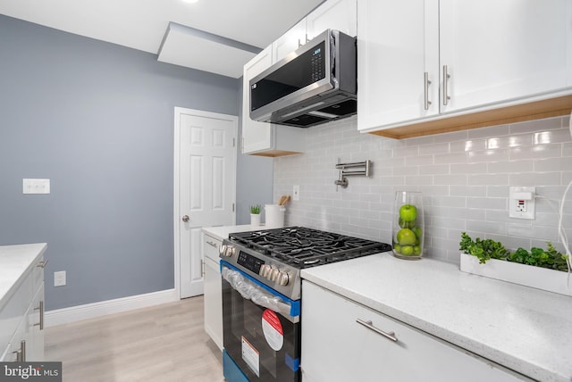 kitchen with decorative backsplash, white cabinetry, light hardwood / wood-style floors, and appliances with stainless steel finishes