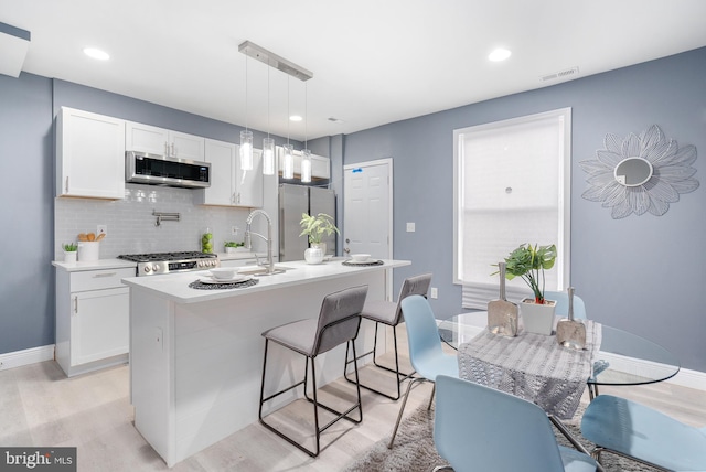 kitchen featuring decorative backsplash, white cabinetry, hanging light fixtures, and appliances with stainless steel finishes