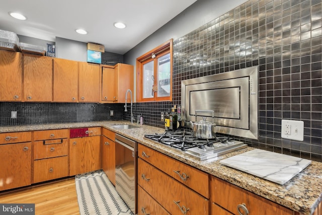 kitchen with sink, light stone countertops, tasteful backsplash, light hardwood / wood-style floors, and stainless steel appliances