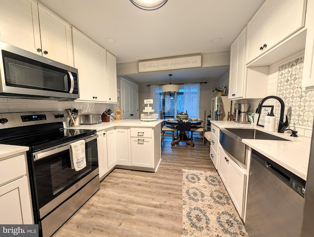 kitchen featuring sink, white cabinets, hanging light fixtures, kitchen peninsula, and stainless steel appliances