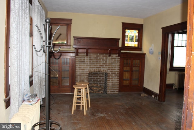 living room featuring radiator heating unit, dark wood-type flooring, and a brick fireplace