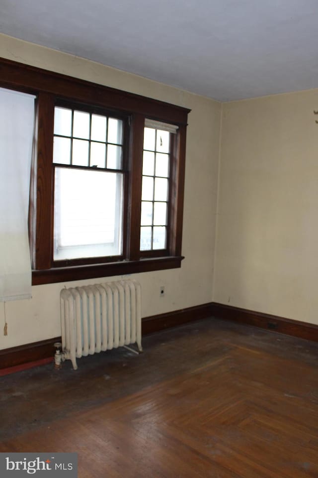 empty room with dark parquet flooring and radiator