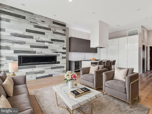 living room featuring wood walls, sink, wine cooler, and light hardwood / wood-style flooring