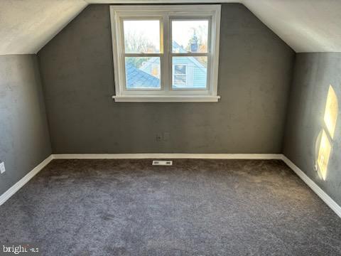 additional living space featuring dark carpet and vaulted ceiling