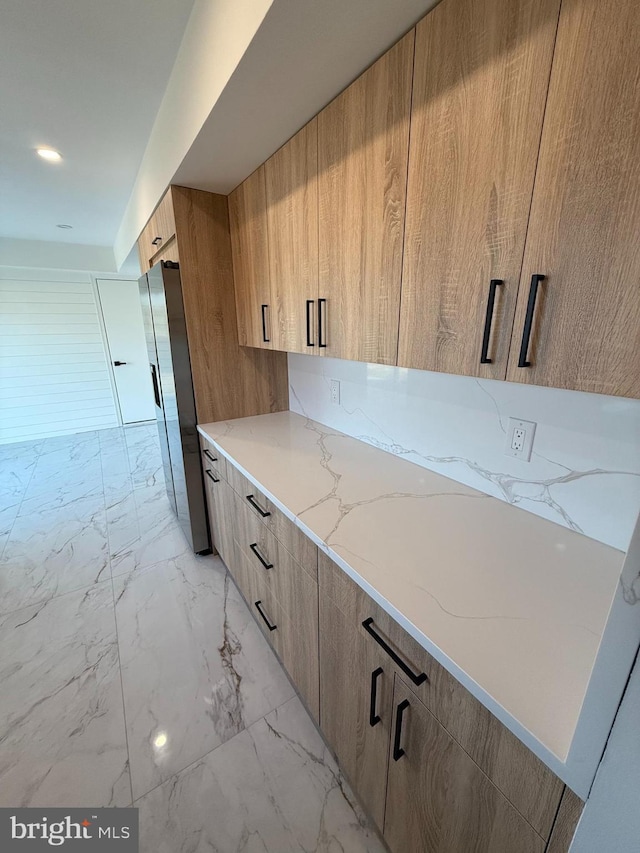 kitchen with stainless steel fridge, light brown cabinets, and light stone counters