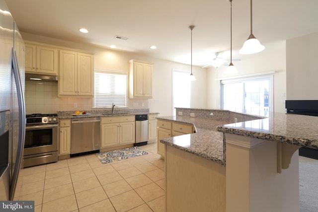 kitchen featuring light stone counters, stainless steel appliances, sink, pendant lighting, and light tile patterned floors