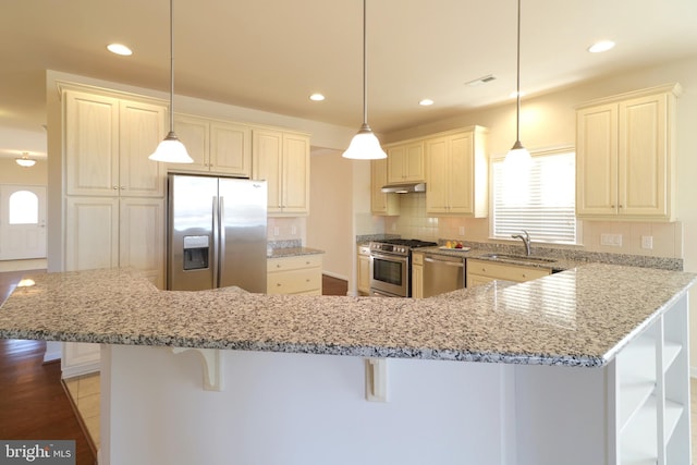 kitchen featuring hanging light fixtures, sink, appliances with stainless steel finishes, and a breakfast bar area