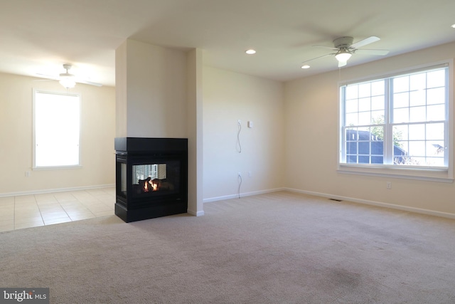 unfurnished living room with a multi sided fireplace, ceiling fan, and light colored carpet