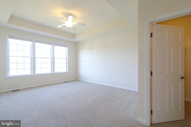 carpeted spare room with a tray ceiling and ceiling fan