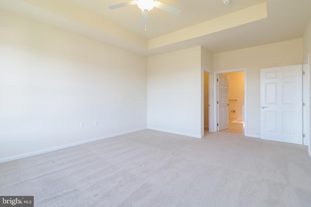 carpeted spare room with a tray ceiling and ceiling fan