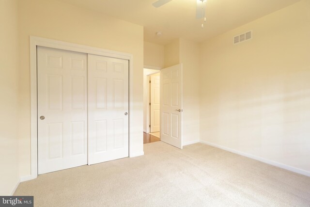 unfurnished bedroom featuring ceiling fan, light colored carpet, and a closet