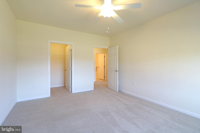 unfurnished bedroom with a closet, a spacious closet, ceiling fan, and light colored carpet