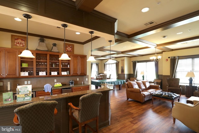 kitchen with a kitchen bar, backsplash, coffered ceiling, decorative light fixtures, and dark stone countertops