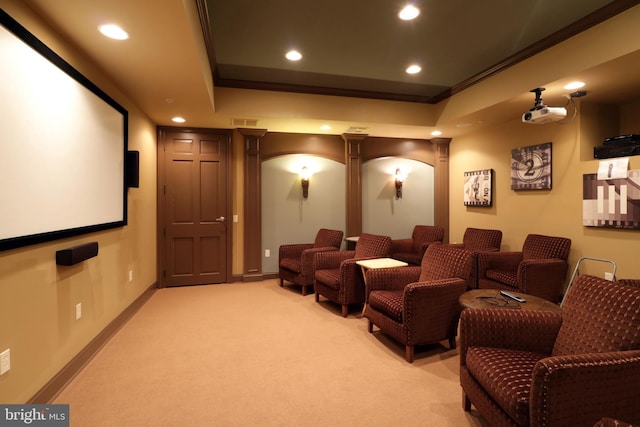 home theater featuring a tray ceiling, ornate columns, light carpet, and ornamental molding