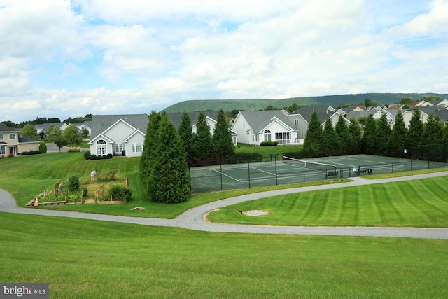 view of property's community featuring a lawn and tennis court