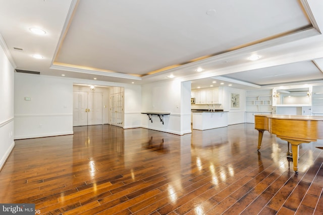 unfurnished living room with ornamental molding, a raised ceiling, built in shelves, and dark wood-type flooring