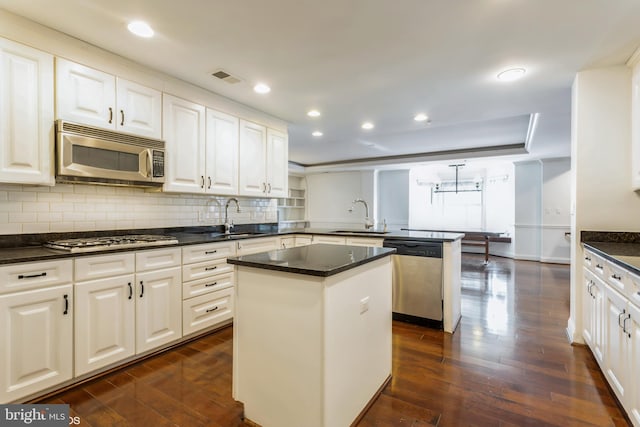 kitchen with sink, a center island, dark wood-type flooring, kitchen peninsula, and appliances with stainless steel finishes