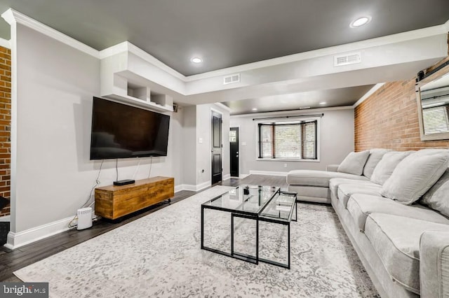 living room featuring dark hardwood / wood-style flooring, crown molding, and brick wall